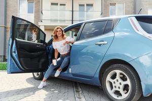 assis dans la voiture. jeune femme en vêtements décontractés avec son électromobile à l'extérieur pendant la journée photo