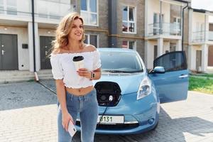 voiture en charge. jeune femme en vêtements décontractés avec son électromobile à l'extérieur pendant la journée photo