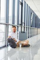 homme assis par terre. le jeune voyageur est dans le hall d'entrée de l'aéroport photo