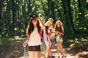 fille debout devant ses amis. enfants se promenant dans la forêt avec équipement de voyage photo