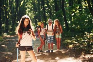 fille debout devant ses amis. enfants se promenant dans la forêt avec équipement de voyage photo