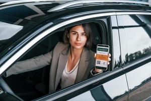 tenant un smartphone avec un passeport de vaccin numérique. femme testant une nouvelle voiture. assis à l'intérieur dans une automobile moderne photo