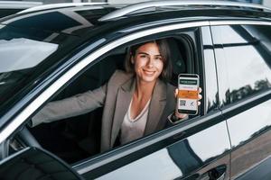 tenant un smartphone avec un passeport de vaccin numérique. femme testant une nouvelle voiture. assis à l'intérieur dans une automobile moderne photo