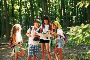 en utilisant la carte pour trouver un chemin. enfants se promenant dans la forêt avec équipement de voyage photo