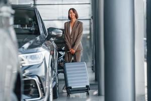 tenue de bagages. la femme est à l'intérieur près d'une nouvelle automobile à l'intérieur photo