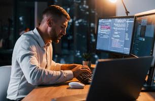 la nuit. jeune homme d'affaires en vêtements formels est au bureau avec plusieurs écrans photo