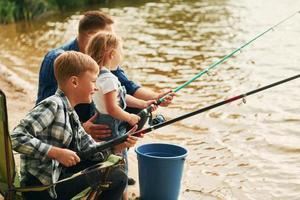 assis ensemble. père avec fils et fille sur la pêche en plein air en été photo