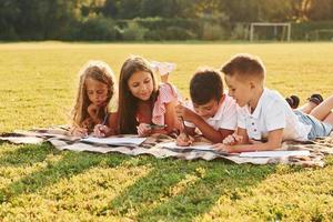 dessiner des images. groupe d'enfants heureux est à l'extérieur sur le terrain de sport pendant la journée photo