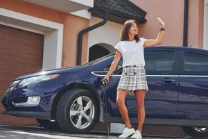 la voiture est sur la borne de recharge électrique. la femme est à l'extérieur avec son automobile moderne photo