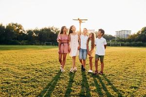 courir avec un avion jouet. groupe d'enfants heureux est à l'extérieur sur le terrain de sport pendant la journée photo