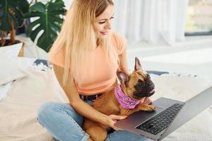 à l'aide d'un ordinateur portable. femme avec chien carlin est à la maison pendant la journée photo