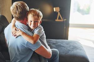 garçon embrassant son parent. père et fils sont à l'intérieur à la maison ensemble photo