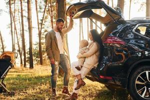 avec automobile de couleur noire. famille heureuse de père, mère et petite fille est dans la forêt photo