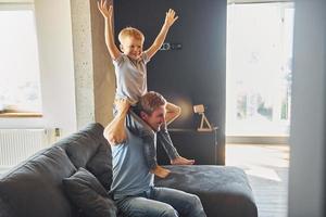 garçon est assis sur les épaules de l'homme. père et fils sont à l'intérieur à la maison ensemble photo