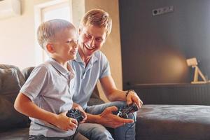 avec des manettes de jeu vidéo. père et fils sont à l'intérieur à la maison ensemble photo