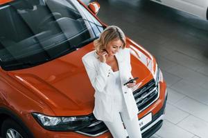 appuyé sur la voiture. femme en vêtements formels est à l'intérieur dans l'autosalon photo