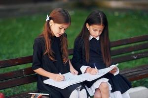 assis et lisant. deux écolières sont dehors ensemble près du bâtiment de l'école photo