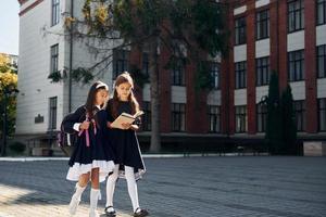 avec des livres. deux écolières sont dehors ensemble près du bâtiment de l'école photo