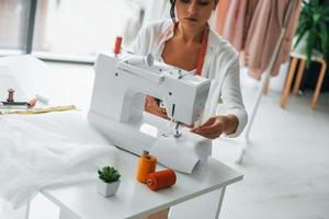 travailler à l'aide d'une machine à coudre. la couturière est dans son bureau avec des vêtements différents photo