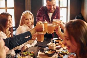 tenant des verres. groupe de jeunes amis assis ensemble au bar avec de la bière photo