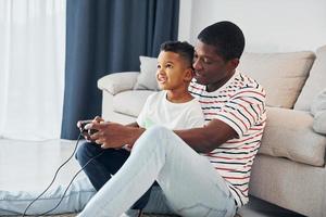 jouer aux jeux-vidéos. père afro-américain avec son jeune fils à la maison photo