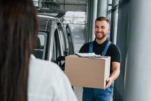 la femme attend sa commande. livreur en uniforme est à l'intérieur avec voiture photo