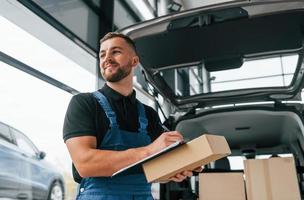 portrait de livreur en uniforme qui est à l'intérieur avec voiture et avec commande photo