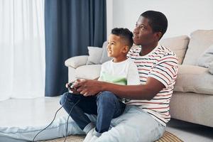 jouer aux jeux-vidéos. père afro-américain avec son jeune fils à la maison photo