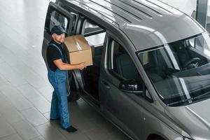 dans des vêtements de couleur bleue. livreur en uniforme est à l'intérieur avec voiture et avec commande photo