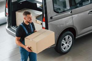 marchant et tenant la boîte dans les mains. livreur en uniforme est à l'intérieur avec voiture et avec commande photo