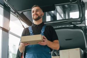 Émotions positives. livreur en uniforme est à l'intérieur avec voiture et avec commande photo