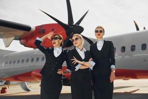 trois hôtesses. équipage de travailleurs de l'aéroport et de l'avion en vêtements formels debout ensemble à l'extérieur photo