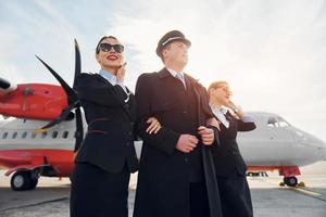 trois personnes. équipage de travailleurs de l'aéroport et de l'avion en vêtements formels debout ensemble à l'extérieur photo