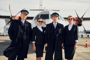 deux hommes et deux femmes. équipage de travailleurs de l'aéroport et de l'avion en vêtements formels debout ensemble à l'extérieur photo