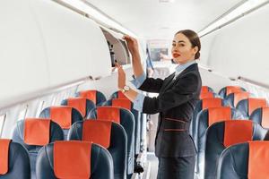 une jeune hôtesse de l'air vêtue de vêtements noirs formels se tient à l'intérieur de l'avion photo