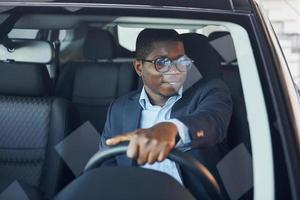 vue de face. jeune homme d'affaires afro-américain en costume noir est dans l'automobile photo