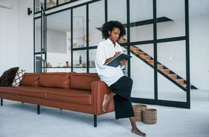 tient le bloc-notes. jeune femme afro-américaine aux cheveux bouclés à l'intérieur à la maison photo