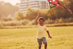 cerf-volant rouge. un enfant afro-américain s'amuse sur le terrain pendant la journée d'été photo