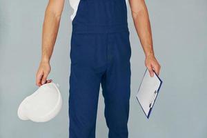 avec bloc-notes et casque. travailleur masculin en uniforme bleu debout à l'intérieur du studio sur fond blanc photo