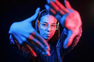 fait des gestes avec les mains. portrait de jeune fille qui porte des lunettes dans un éclairage au néon bleu photo