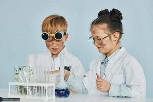 fille avec garçon travaillant ensemble. des enfants en blouse blanche jouent un scientifique en laboratoire en utilisant un équipement photo
