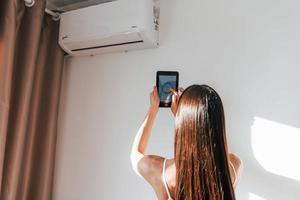 vue arrière d'une femme qui se tient à l'intérieur avec un téléphone et contrôle la technologie de la maison intelligente photo