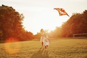 la femme aide la fille à contrôler le cerf-volant. mère et fille s'amusent sur le terrain. belle nature photo