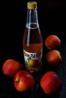 krasnoyarsk, russie - 09 juin 2022 une bouteille de cidre de pomme de bonne saison en gouttes d'eau et de pommes rouges sur fond sombre. photo