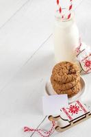 bouteille de lait, biscuits, note vierge, mitaines décoratives, traîneau sur des planches diagonales en bois blanc. Noël. photo