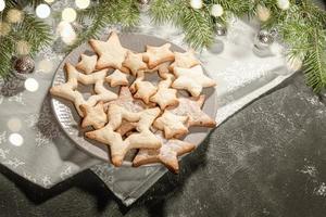 assiette avec des biscuits festifs en forme d'étoiles sur une serviette grise sur fond noir avec des lumières bokeh. photo