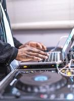 dj joue en direct et mixe de la musique sur un ordinateur portable. disque jokey mains sur un ordinateur portable au club. photo