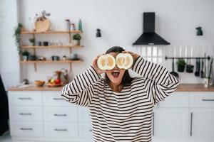 une femme tient des fruits coupés au niveau des yeux au lieu de lunettes photo