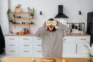 une femme tient des fruits coupés au niveau des yeux au lieu de lunettes photo