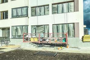 construction d'un nouveau microquartier en centre-ville. maison en béton blanc. peindre les murs, dans le berceau de la grue, le peintre travaille avec la façade de la maison photo